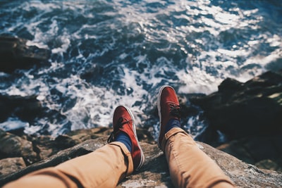 穿着红色运动鞋的男子坐在靠近水体的悬崖上